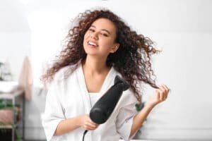 beautiful young woman blow drying curly hair