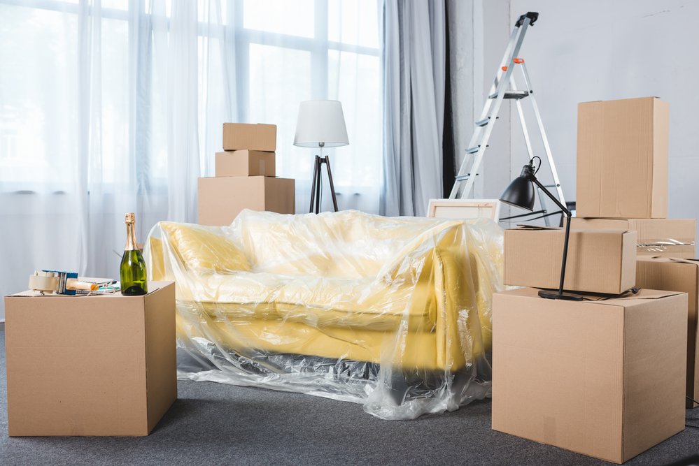 Empty living room with platic-wrapped couch and stacks of boxes